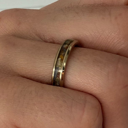 A close-up of a hand wearing a gold band ring with an inlay of small amber or honey-colored pieces.