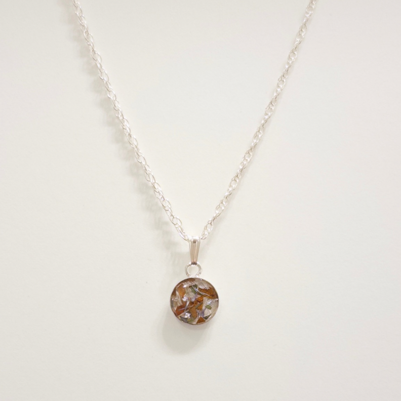 A silver chain necklace with a small round pendant featuring a brown and gray marbled pattern, displayed against a plain off-white background.