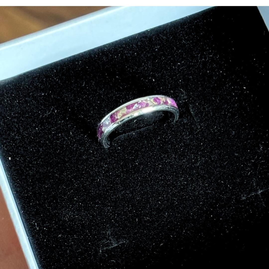 A silver band ring with a row of pink dried flowers, displayed on a black velvet jewelry box.