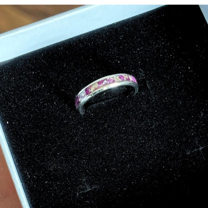 A silver band ring with a row of pink dried flowers, displayed on a black velvet jewelry box.
