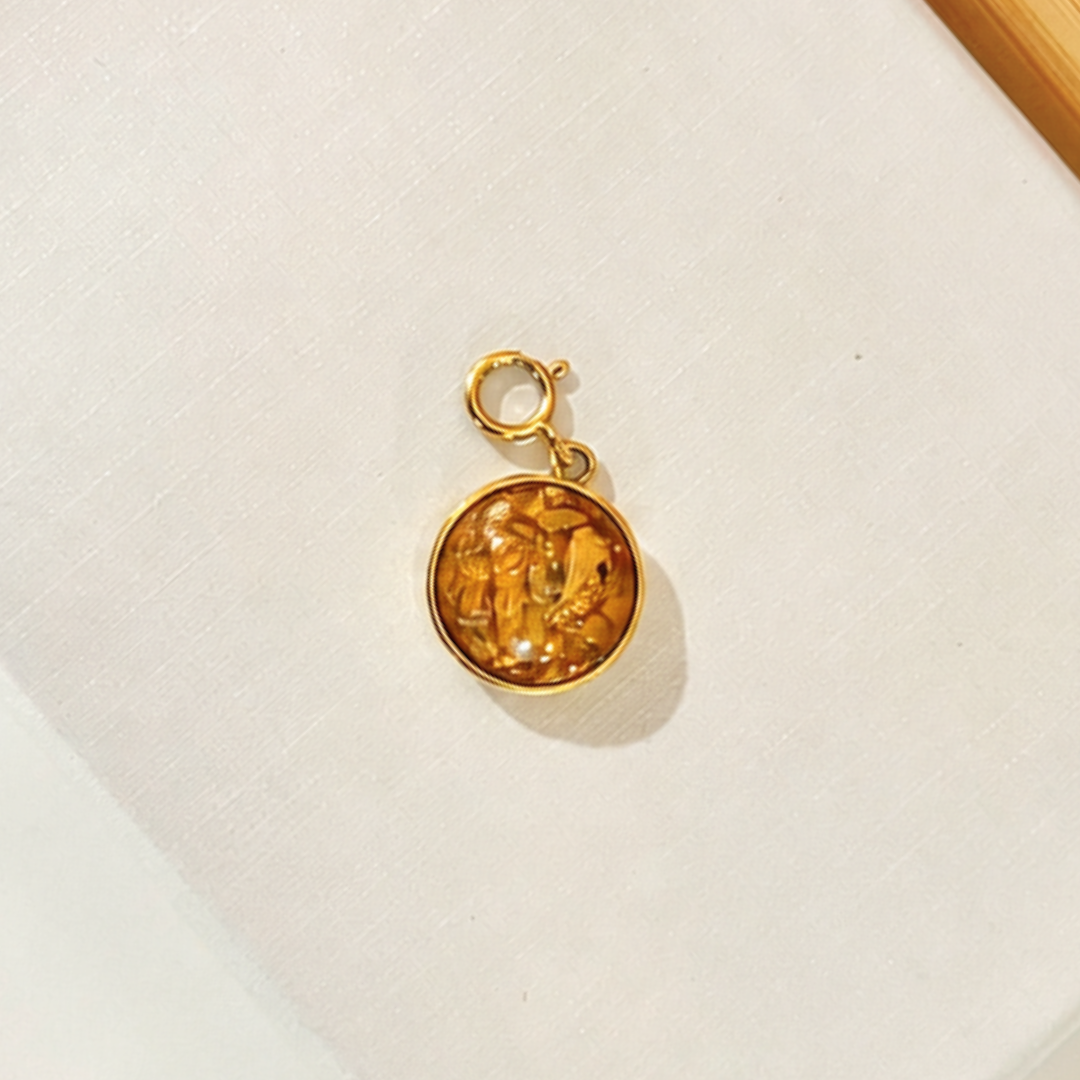 A circle gold pendant filled with dried white and yellow rose petals and gold flakes encased in resin with a clasp. It sits on a textured white background.