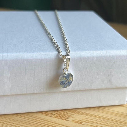 A silver chain necklace with a round pendant featuring a blue and gold abstract pattern, resting on a white textured box.